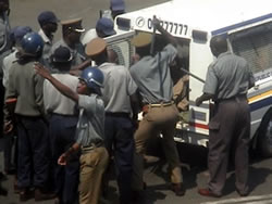 Police beat the legs and feet of the protestors as they are forced into the vehicle